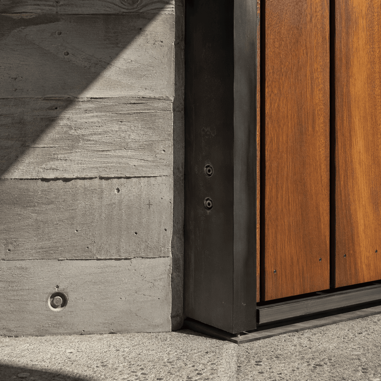 Precise junction of concrete, blackened steel and warm timber